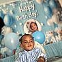 background, balloons, birthday, blue, bracelet, celebration, child, clothing, cute, decorations, event, face, happy, high_chair, indoor, party, person, portrait, smile, toddler