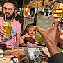baby, beard, beverage, black_hair, brown_skin, cheers, drink, drinking_straw, facial_hair, food, glasses, hand, indoor, menu, person, restaurant, table, woman, wood, young_child