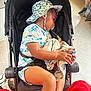 blanket, candid, casual, child, clothing, colorful, comfort, face, footwear, hand, hat, indoor, pacifier, person, resting, seat, stroller, toddler, toy, young_child