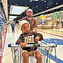 adult, aisle, beige_shorts, cap, casual_clothing, child, floor, focus, glasses, grocery_store, hat, indoor, lighting, person, retail, shopping, shopping_cart, sneakers, supermarket, sweatshirt