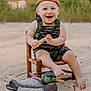 toddler, child, smiling, cap, brown_cap, overalls, camouflage, wooden_chair, sand, toy, wooden_toy, duck_decoy, outdoor, nature, greenery, happy, barefoot, portrait, seat, summer