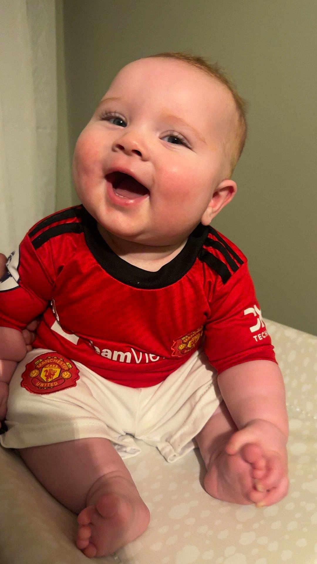 Wyatt joined the competition — help win amazing prizes! baby, child, smiling, happy, red_jersey, manchester_united, sportswear, shorts, barefoot, indoor, portrait, cute, cheerful, infant, sitting, head, face, person, skin, clothing