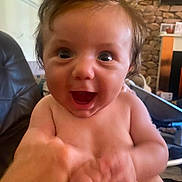 Archie is registered to the contest to win money with this photo: baby, child, closeup, expression, face, fireplace, furniture, hair, hand, human, indoor, infant, interaction, joy, laugh, living_room, person, skin, smile, stone_wall