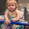 Delilah joined the competition — help win amazing prizes! baby, child, toddler, shopping_cart, grocery_store, indoor, portrait, sitting, serious_expression, blue_eyes, blonde_hair, ponytail, floral_shirt, blanket, barefoot, cart, aisle, hallway, fire_extinguisher, painting