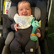 Oscar is registered to the contest to win money with this photo: baby, car_seat, smiling, bib, plush_toy, elephant_toy, onesie, blanket, infant, child, happy, indoor, seatbelt, head_support, clothing, toy, person, portrait, cute, comfort