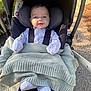 baby, infant, stroller, blanket, clothing, outdoor, sunlight, happy, smile, face, person, seat, safety_harness, footwear, nature, pavement, head_support, cute, child, warm