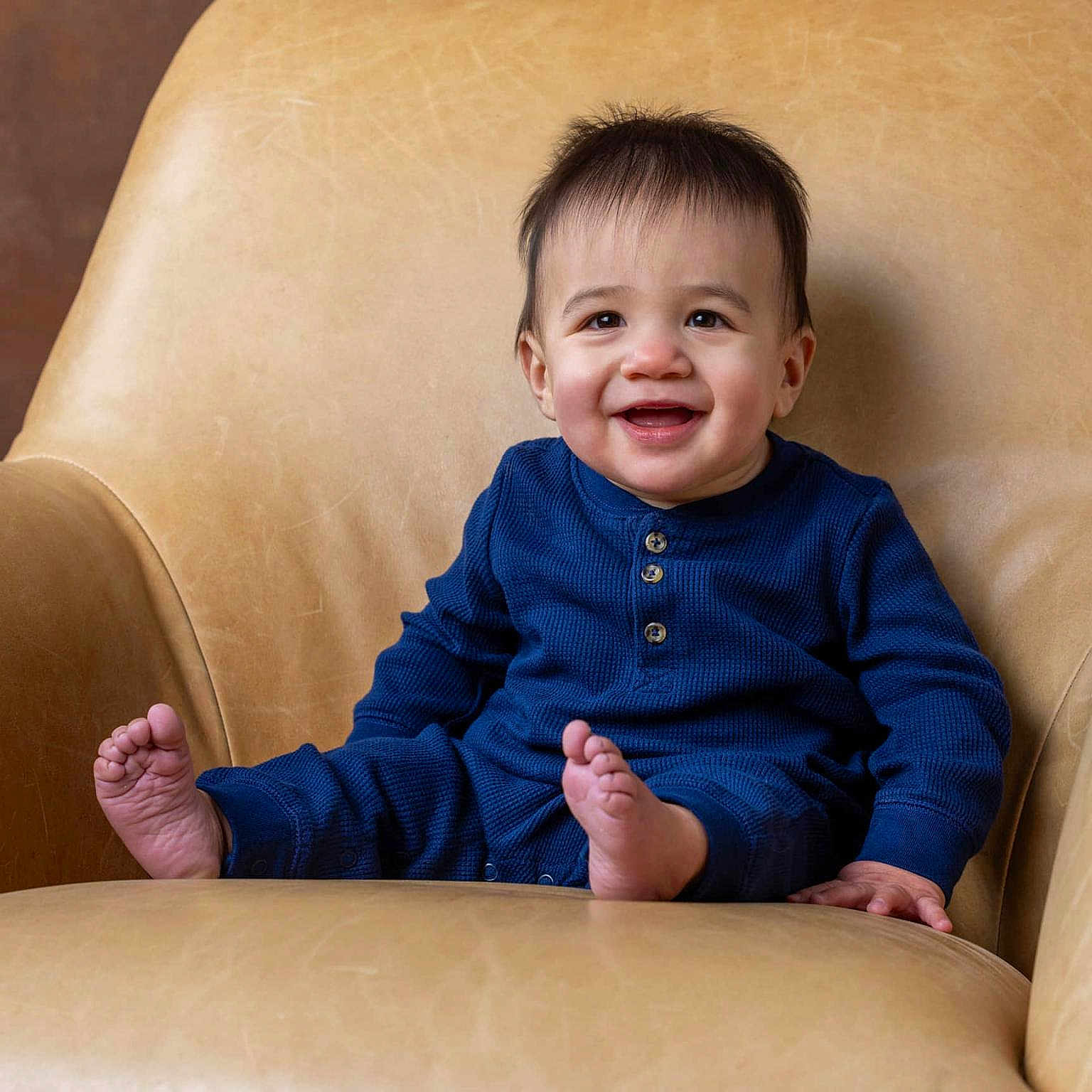 Lucian is registered to the contest to win money with this photo: baby, barefoot, blue_clothing, casual_wear, child, cozy, cute, furniture, happy, human, indoor, infant, leather_chair, portrait, seated, sitting, small_child, smiling, warm_colors, young_child