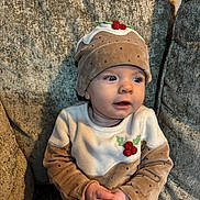 Darcy Mae joined the competition — help win amazing prizes! baby, child, christmas_pudding_hat, clothing, couch, cozy, cushion, cute, expression, face, festive, furniture, hands, holiday_outfit, indoor, infant, looking_away, plush, sitting, soft_lighting