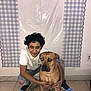 person, dog, indoor, floor, curly_hair, white_shirt, ripped_jeans, blue_shoes, tile_floor, wall, decor, hugging, pet, animal, casual_clothing, smiling, portrait, companion, friendship, crouching