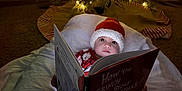 Alexander is registered to the contest to win money with this photo: baby, blanket, book, child, christmas_lights, christmas_tree, cozy, cute, face, festive, floor, holiday, indoors, pajamas, portrait, reading, santa_hat, seasonal, storybook, winter