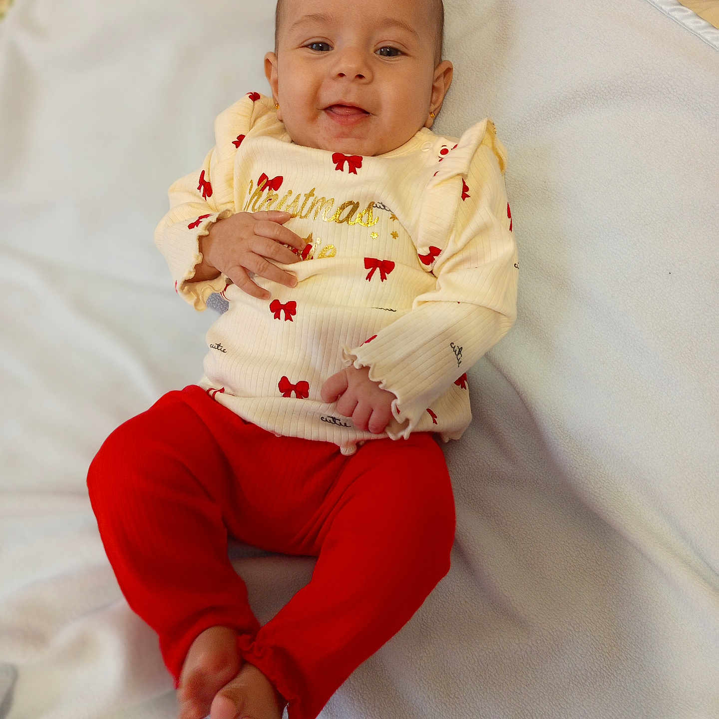 Iris is registered to the contest to win money with this photo: baby, blanket, bows, child, cozy, cream_sweater, cute, face, feet, hands, happy, indoors, infant, lying_down, person, portrait, red_pants, smiling, soft_texture, warm_clothing