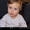 toddler, child, portrait, face, blue_eyes, blond_hair, white_shirt, sitting, indoors, couch, furniture, cozy, looking_at_camera, neutral_expression, close_up, photography, film_frame, home, baby, people