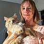 Goldie joined the competition — help win amazing prizes! woman, cat, indoor, smile, fluffy_cat, orange_cat, short_hair, natural_light, holding, pet, face, casual_clothing, portrait, happy, feline, domestic_animal, relaxed, home, cute, cozy