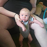 Jasper is registered to the contest to win money with this photo: baby, infant, person, adult, cactus_onesie, blue_eyes, indoor, couch, carpet, sitting, holding, legs, arms, casual_clothing, relaxing, living_room, curious_expression, skin, hand, foot