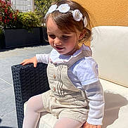 Natacha participe au concours pour gagner de l'argent avec cette photo : child, girl, outdoor, sunlight, headband, white_clothing, overalls, tights, sandals, chair, cushion, pavement, plants, flower, smiling, portrait, daylight, shadow, fence, relaxing