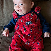 Jaxson joined the competition — help win amazing prizes! baby, child, smiling, red_overalls, toy_soldier_pattern, black_sneakers, couch, seated, indoors, happy, face, clothing, footwear, cute, infant, person, portrait, young_child, apparel, fabric
