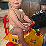 baby, child, toy_airplane, elmo, band_aids, diaper, indoor, kitchen, red_wheel, yellow_toy, smiling, happy, cute, playing, plastic_toy, floor, wooden_cabinet, window, face, person
