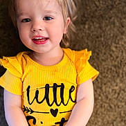 Hailee is registered to the contest to win money with this photo: child, toddler, yellow_clothing, smiling, face, person, carpet, sitting, happy, indoor, cute, portrait, young_child, bright_colors, casual_clothing, baby, childhood, expression, human, playful