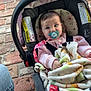 baby, pacifier, car_seat, blanket, brick_floor, jeans, slippers, child, infant, pink_clothing, seatbelt, face, indoors, person, cute, young_child, comfort, patterned_blanket, sitting, closeup
