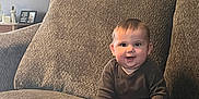 Oaklee is registered to the contest to win money with this photo: baby, child, smile, couch, living_room, family_photos, home_decor, seated, indoors, cozy, cute, happy, infant, furniture, portrait, casual_clothing, feet, hands, wall_art, soft_lighting
