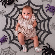 Aminah is registered to the contest to win money with this photo: baby, infant, child, portrait, halloween, spiderweb, plush_spiders, costume, romper, pacifier, smiling, lying_down, indoor, flat_lay, textile, striped_socks, pink_clothing, gray_background, festive, photography