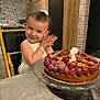 birthday_cake, bracelet, cake, candle, celebration, child, clapping, dessert, food, happy, high_chair, indoor, kitchen, person, raspberries, smile, stone_wall, table, toddler, wood