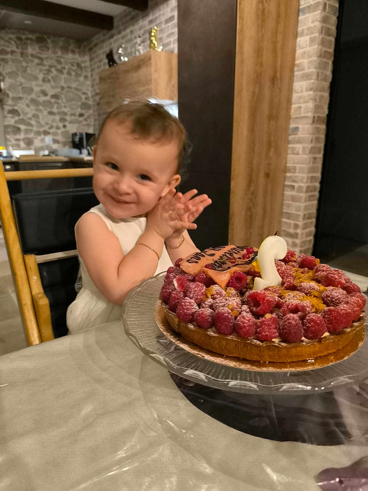 Lycia participe au concours pour gagner de l'argent avec cette photo : birthday_cake, bracelet, cake, candle, celebration, child, clapping, dessert, food, happy, high_chair, indoor, kitchen, person, raspberries, smile, stone_wall, table, toddler, wood