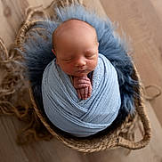 Blaze joined the competition — help win amazing prizes! newborn, baby, swaddled, blue_wrap, basket, woven_basket, fluffy_fur, sleeping, peaceful, wooden_floor, infant, portrait, cute, hands_folded, soft_texture, resting, cozy, indoors, closeup, child