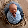newborn, baby, swaddled, blue_wrap, basket, woven_basket, fluffy_fur, sleeping, peaceful, wooden_floor, infant, portrait, cute, hands_folded, soft_texture, resting, cozy, indoors, closeup, child