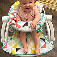 Clara is registered to the contest to win money with this photo: baby, smiling, baby_walker, pink_clothing, cherries, toys, floor, wooden_floor, colorful, happy, child, indoor, footwear_none, person, infant, seat, playful, cute, face, home
