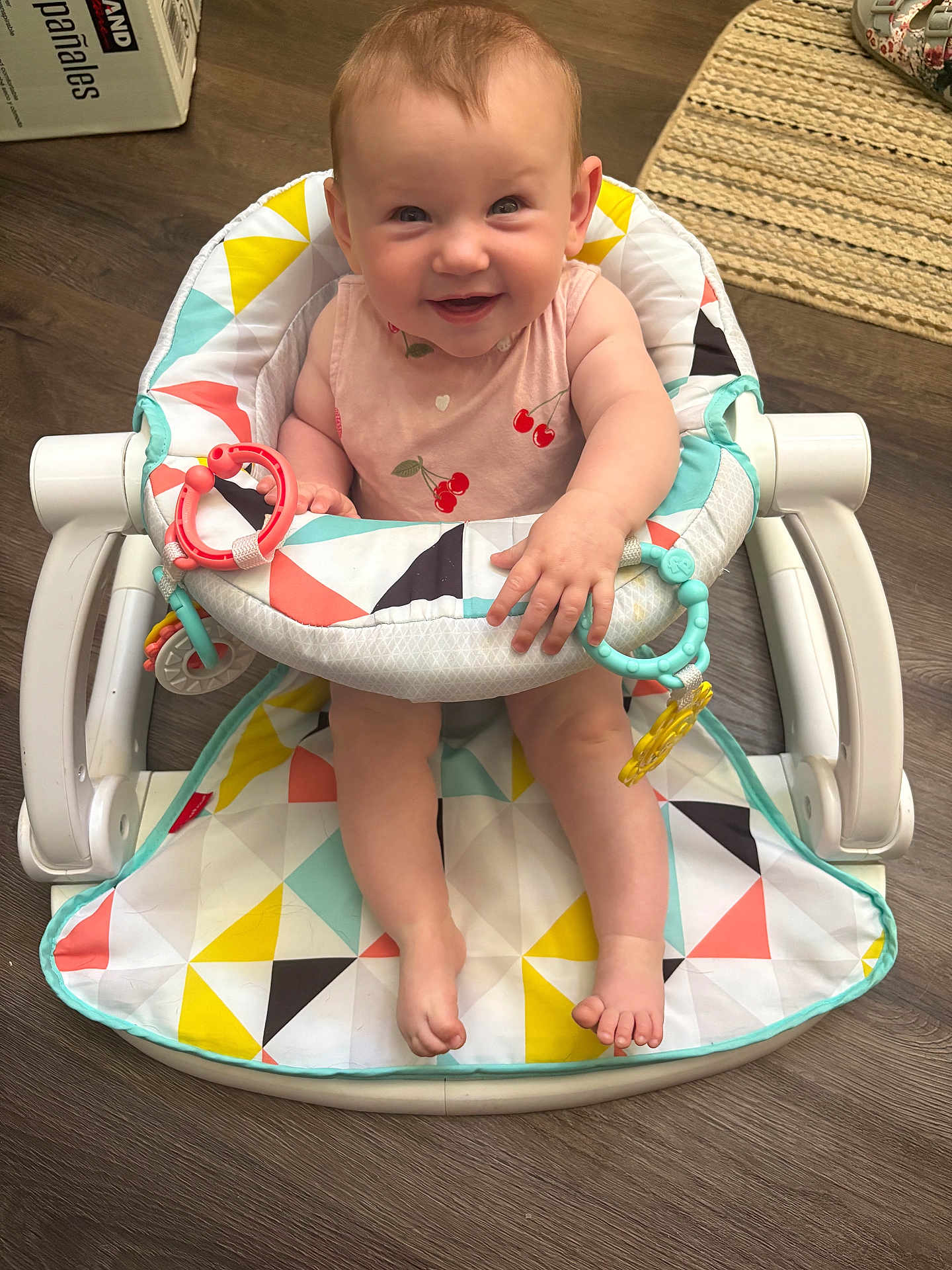 Clara is registered to the contest to win money with this photo: baby, smiling, baby_walker, pink_clothing, cherries, toys, floor, wooden_floor, colorful, happy, child, indoor, footwear_none, person, infant, seat, playful, cute, face, home