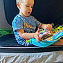 Brandon Jr is registered to the contest to win money with this photo: bodypart, boy, child, clothing, face, finger, furniture, head, indoors, interiordesign, male, openingpresent, person, photography, portrait, reading, sitting, sleeve, t_shirt, text