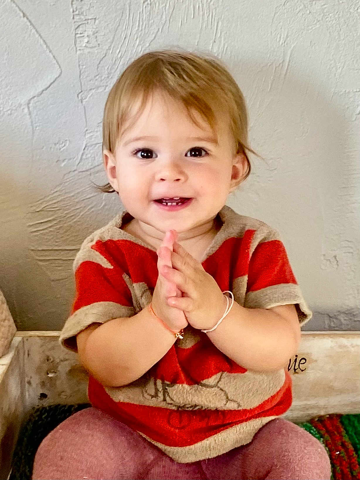 Jeanne participe au concours pour gagner de l'argent avec cette photo : toddler, child, clapping, smiling, happy, indoor, cute, person, face, eyeshiny, hair, sitting, shirt, pants, hands, skin, wall, texture, bracelet, portrait