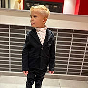 Nùno participe au concours pour gagner de l'argent avec cette photo : background, black_blazer, blonde_hair, casual, child, confident, curious, fashion, footwear, indoor, kid, modern, person, portrait, short_hair, standing, tile_floor, wall, white_turtleneck, young