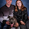animal, blue_background, cap, casual_clothing, dog, friendship, glasses, happy, indoor, jeans, knitted_blanket, leather_jacket, man, people, pet, portrait, sitting, smiling, studio, woman