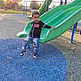 autumn, black_jacket, blue_rubber_floor, casual_clothing, child, childhood, curious_expression, daylight, fun, green_slide, jeans, leisure, outdoor, park, playground, recreation, slide, sneakers, trees, young_boy