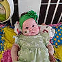 baby, infant, child, headband, green_headband, flower, dress, floral_dress, crib, railings, blanket, quilt, colorful_bedding, pillow, feeding_tube, medical_tape, cheeks, portrait, toy, plush_toy