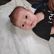 Jace is registered to the contest to win money with this photo: baby, infant, face, child, towel, clothing, person, skin, head, laying, resting, young, cute, indoors, human, portrait, newborn, expression, babywear, soft