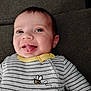 baby, child, tongue_out, smiling, striped_clothing, yellow_collar, onesie, bee_design, pocket, lying_down, soft_surface, happy, cute, infant, face, head, eyes, ears, mouth, person