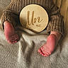 baby, feet, knitwear, brown_clothing, blanket, wooden_plaque, milestone, infant, cozy, texture, closeup, soft_lighting, child, newborn, cuteness, lying_down, warm_colors, skin, small_feet, baby_clothes