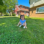 Clarette Amelia is registered to the contest to win money with this photo: child, girl, pigtails, blue_dress, grass, lawn, outdoor, house, suburban, daylight, smile, crouching, greenery, sky, tree, shoes, sidewalk, window, satellite_dish, sunlight