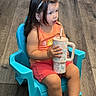 Clarette joined the competition — help win amazing prizes! child, girl, plastic_chair, blue_chair, tumbler, drinking_cup, flooring, wood_floor, indoor, casual_clothing, orange_shirt, pink_shorts, hairband, long_hair, barefoot, portrait, sitting, young_child, curious_expression, home_interior