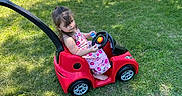 Clarette is registered to the contest to win money with this photo: child, girl, toy_car, grass, outdoor, sunlight, people, festival, fair, dress, barefoot, red, green, summer, play, event, crowd, shadow, fun, park