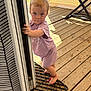 ankle_bracelet, baby, barefoot, casual, child, curious, daylight, door_frame, home, mat, outdoor, person, playful, portrait, purple_clothing, standing, summer, sunlight, toddler, wooden_deck