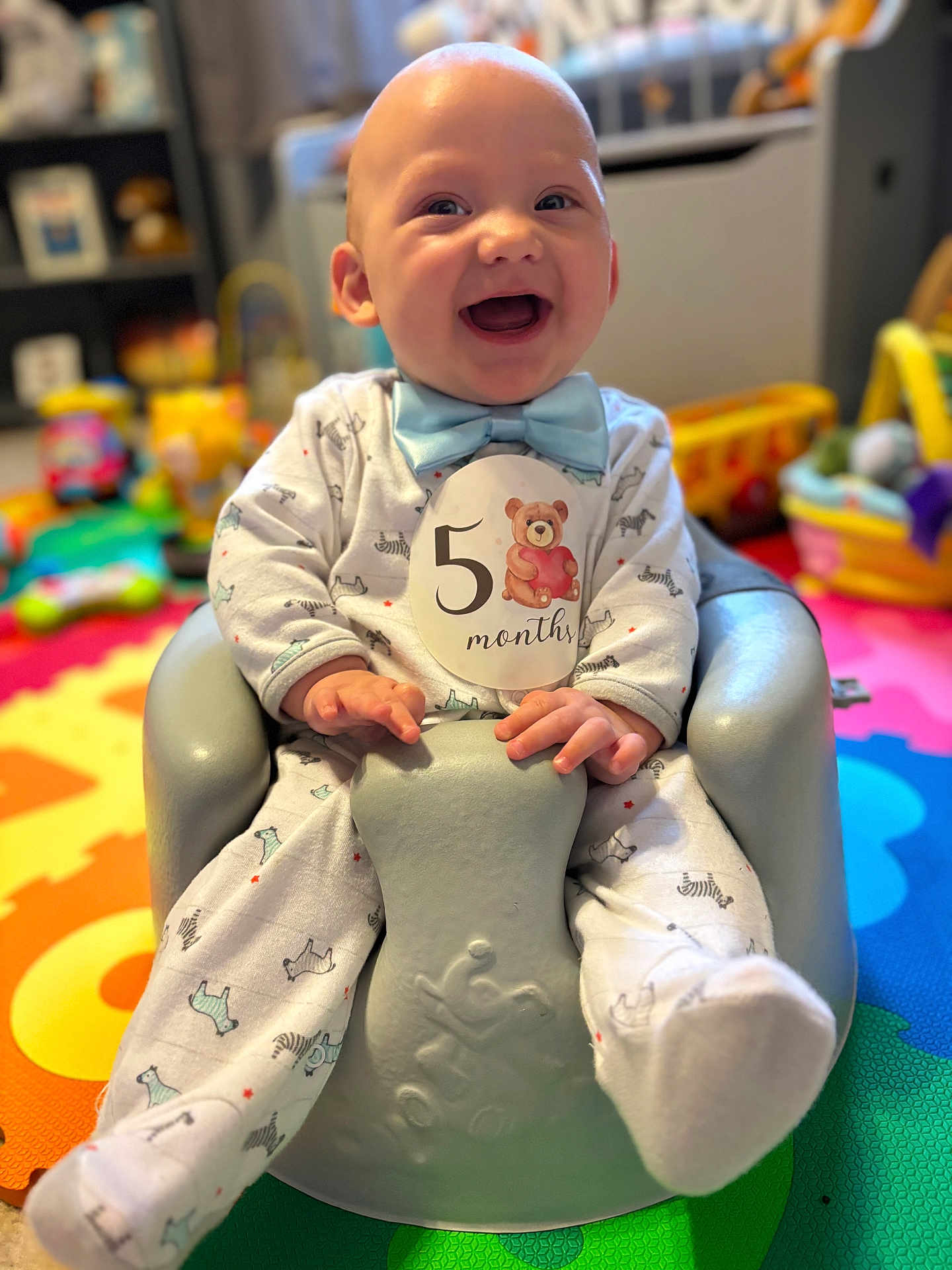 Landon is registered to the contest to win money with this photo: baby, infant, smiling, blue_bow_tie, onesie, baby_seat, play_mat, toys, indoor, child, happy, cute, sitting, colorful, portrait, young_child, soft_lighting, home, fun, cheerful