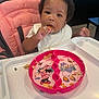 Cherish is registered to the contest to win money with this photo: toddler, child, high_chair, food, snack, plate, pink, minnie_mouse, daisy_duck, messy, curly_hair, bib, indoor, table, person, eating, face, hand, expression, seat