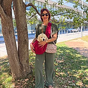 Belly a rejoint le concours — aidez-le/la à gagner de superbes lots ! bag, building, casual_clothing, daytime, dog, grass, green_pants, holding, leaves, nature, outdoor, pet, puppy, sidewalk, smile, sunglasses, sunlight, tree, urban, woman