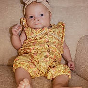 Iris participe au concours pour gagner de l'argent avec cette photo : baby, infant, child, headband, bow, yellow_clothing, floral_pattern, couch, beige, soft_texture, barefoot, portrait, cute, indoor, small_hands, small_feet, relaxed, looking_at_camera, comfortable, seated