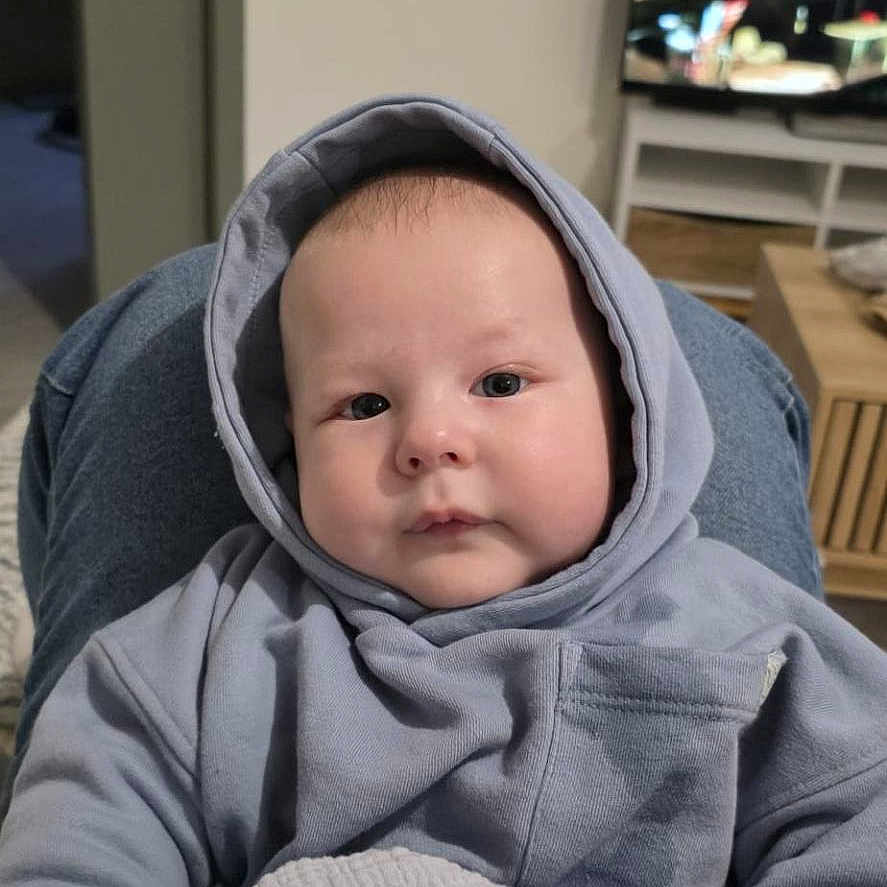 Timiarii participe au concours pour gagner de l'argent avec cette photo : baby, blanket, blue, casual_clothing, child, cozy, curious, face, furniture, hands, home, hoodie, indoor, living_room, person, portrait, seated, soft_texture, television, young_child