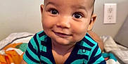Zeke is registered to the contest to win money with this photo: baby, child, smiling, striped_shirt, blanket, indoor, cute, playful, portrait, skin, face, hands, infant, young_child, happy, lying_down, colorful, patterned, room, electric_outlet
